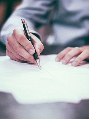 A document being signed, you can only see the hands holding a pen over paperwork.